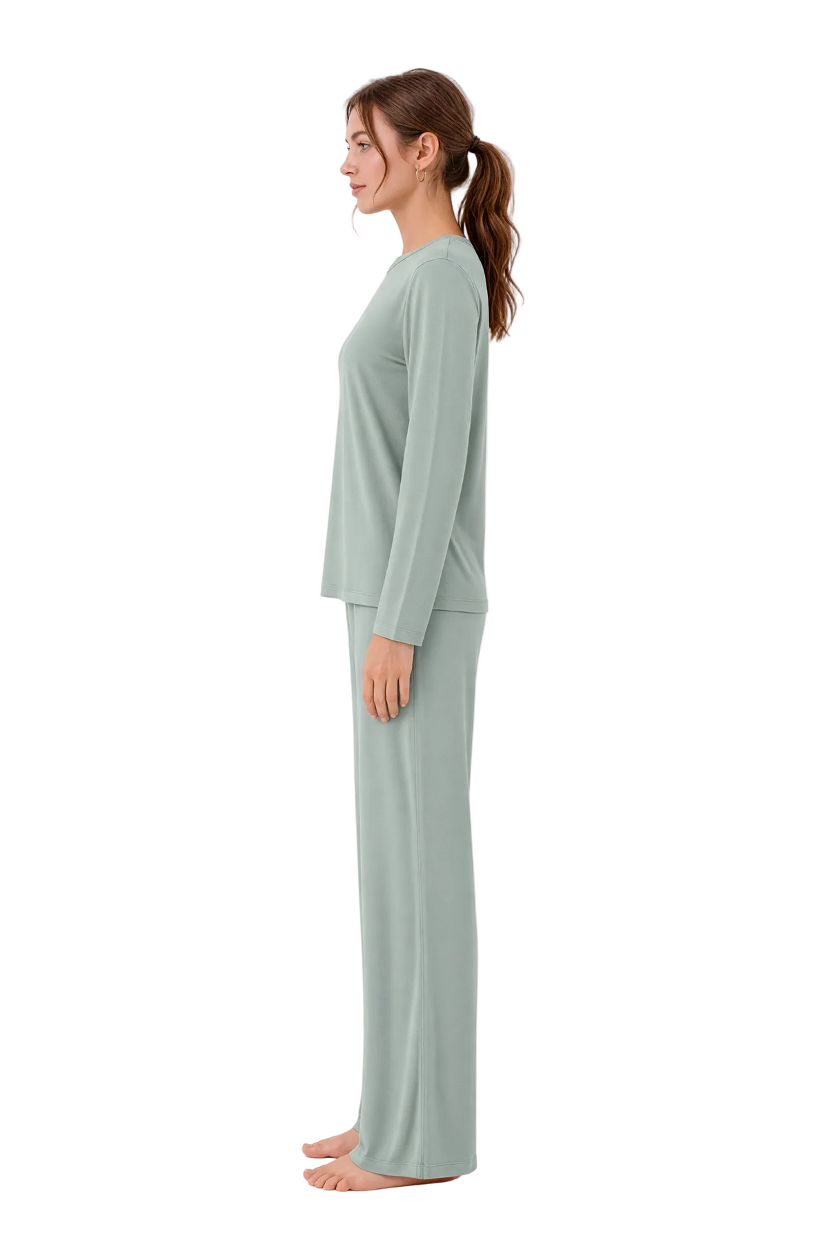A woman stands in profile wearing a matching two-piece lounge set consisting of a long-sleeve top and wide-leg pants in a soft sage green color, set against a plain white studio background.