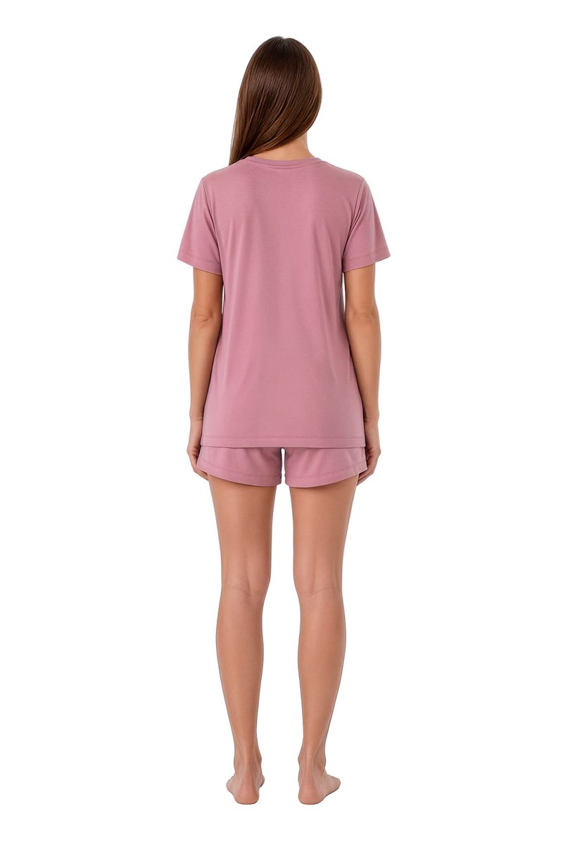 A woman viewed from the back wearing a dusty pink short-sleeve pajama top and matching shorts against a plain white background.