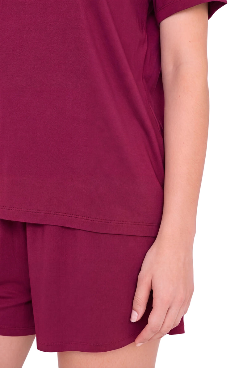 A close-up of a person wearing a matching burgundy short-sleeve top and shorts set, showing the side profile and hand against a plain light background.